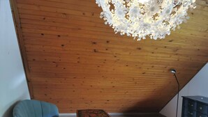 Una habitación con techo de madera, un sillón azul, una mesita con diseño floral y un aparador.