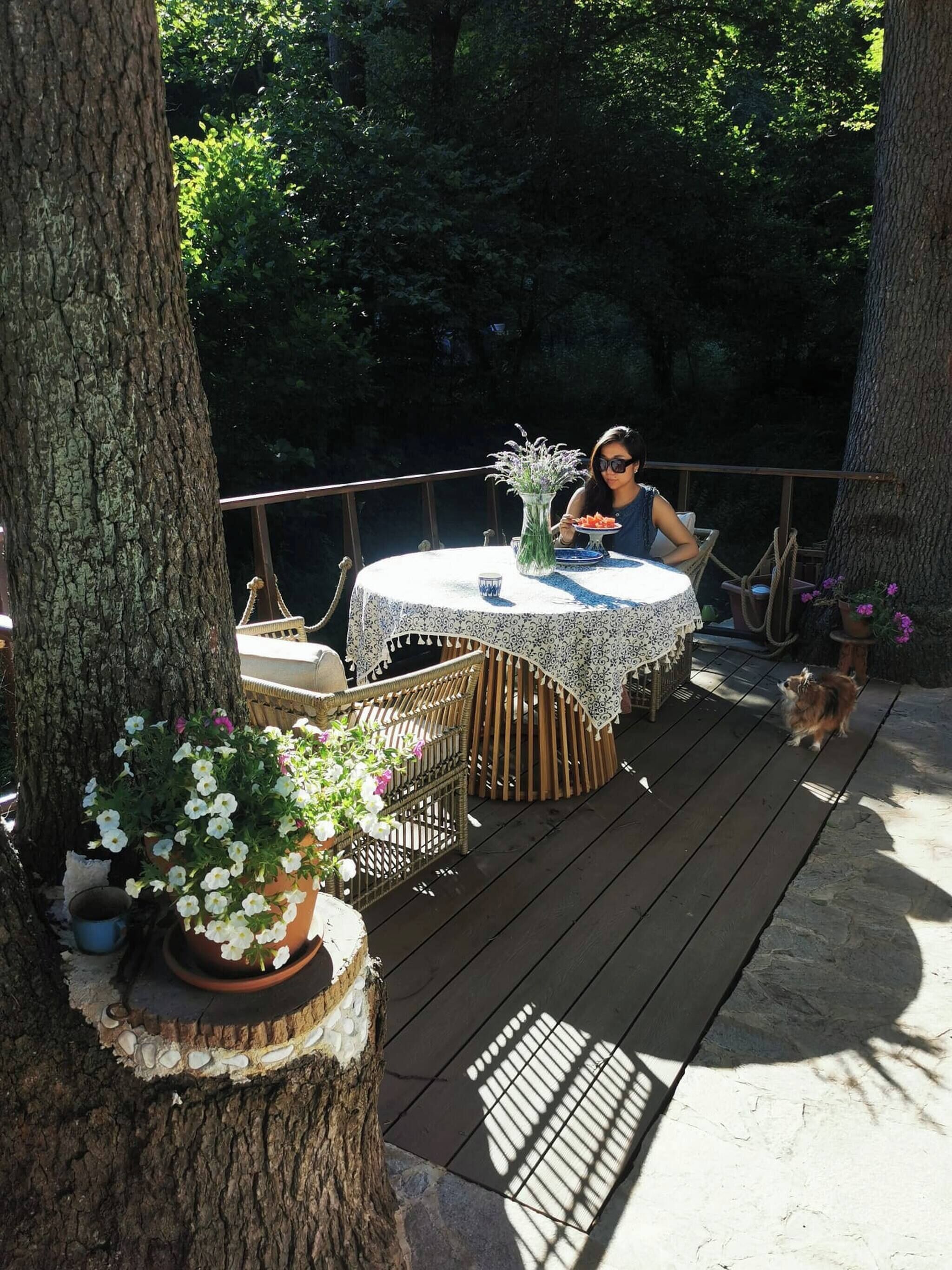 A wooden deck with a round table and chairs, surrounded by trees.