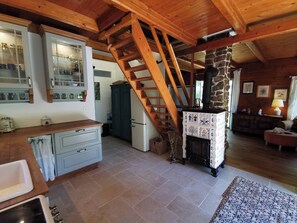 Una cocina rústica con una escalera de madera, una chimenea de piedra y un comedor con mesa y sillas.