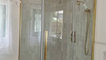 A glass-enclosed shower with a gold frame, tiled walls, and a wooden ceiling beam.