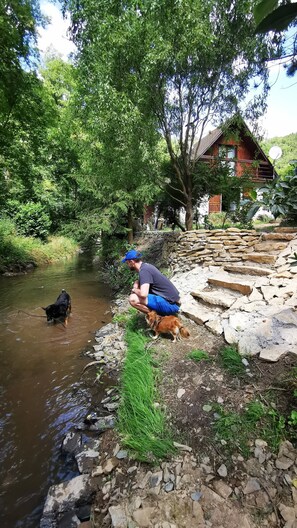 A rustic stone bridge over a river, a wooden cabin in the background, and a person with a dog by the water. - Fairy Tale Cottage on Water Stream, 30 Minutes From South Prague (Petrov)