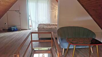 Un dormitorio tipo loft con techo inclinado, una cama con colcha estampada de flores, un sillón verde, una mesita con estampado floral y un banco de madera.