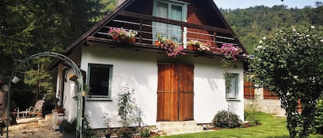 A two-story house with a sloped roof, wooden balcony with flower boxes, and a stone staircase leading to the entrance.
