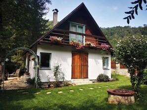 Una casa a due piani con tetto spiovente, un balcone in legno con fioriere e una scala in pietra che conduce all'ingresso.