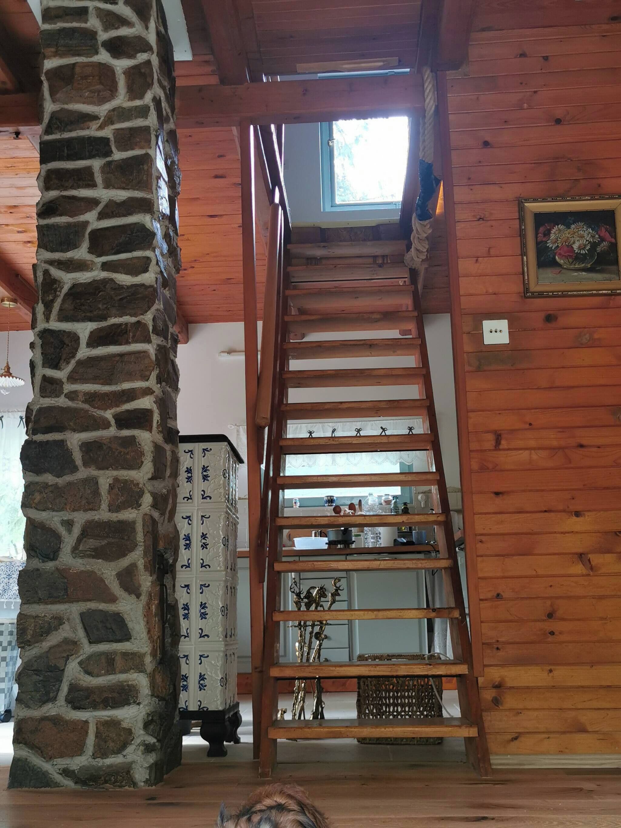 A wooden interior with a stone pillar, a wooden ladder, and a window.