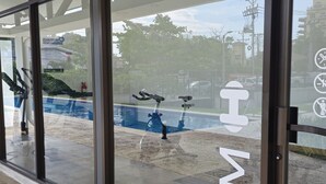 A gym entrance with large glass doors, a concrete floor, and a view of a swimming pool and buildings in the background. - Modern Beach Condo, Jaco (Jacó)
