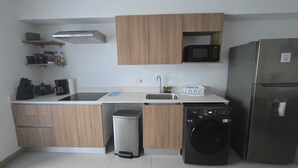 A compact kitchen with a sink, microwave, dishwasher, and wooden cabinets. - Modern Beach Condo, Jaco (Jacó)