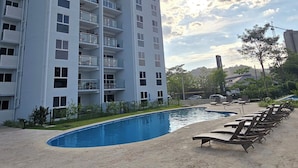 A high-rise building with multiple balconies, a swimming pool, and lounge chairs. - Modern Beach Condo, Jaco (Jacó)