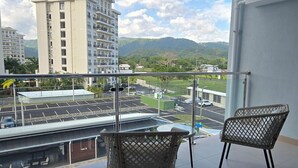 A balcony with two wicker chairs, a view of a parking lot, and a building in the background. - Modern Beach Condo, Jaco (Jacó)
