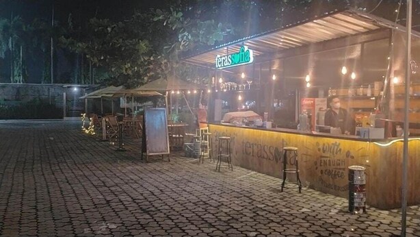 Un café al aire libre con un mostrador amarillo, taburetes y un letrero de neón.