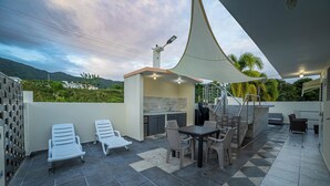 A covered outdoor patio with a table and chairs, a grill, and a seating area with lounge chairs. - Jesus did it, Christian Paradise with jacuzzi, terrace, and peaceful atmosphere. (Patillas)