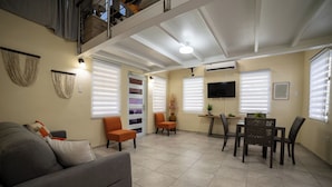 A living room with a sofa, two orange chairs, a dining table with chairs, and a TV on the wall. - Jesus did it, Christian Paradise with jacuzzi, terrace, and peaceful atmosphere. (Patillas)