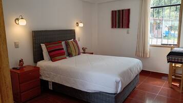 A bedroom with a large bed, two bedside tables, a nightstand, a window with curtains, and a wall-mounted artwork.