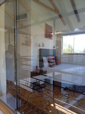 A bedroom with a bed, bedside table, lamp, and a view of the outdoors. - Sueños del Valle Sagrado (Urubamba)