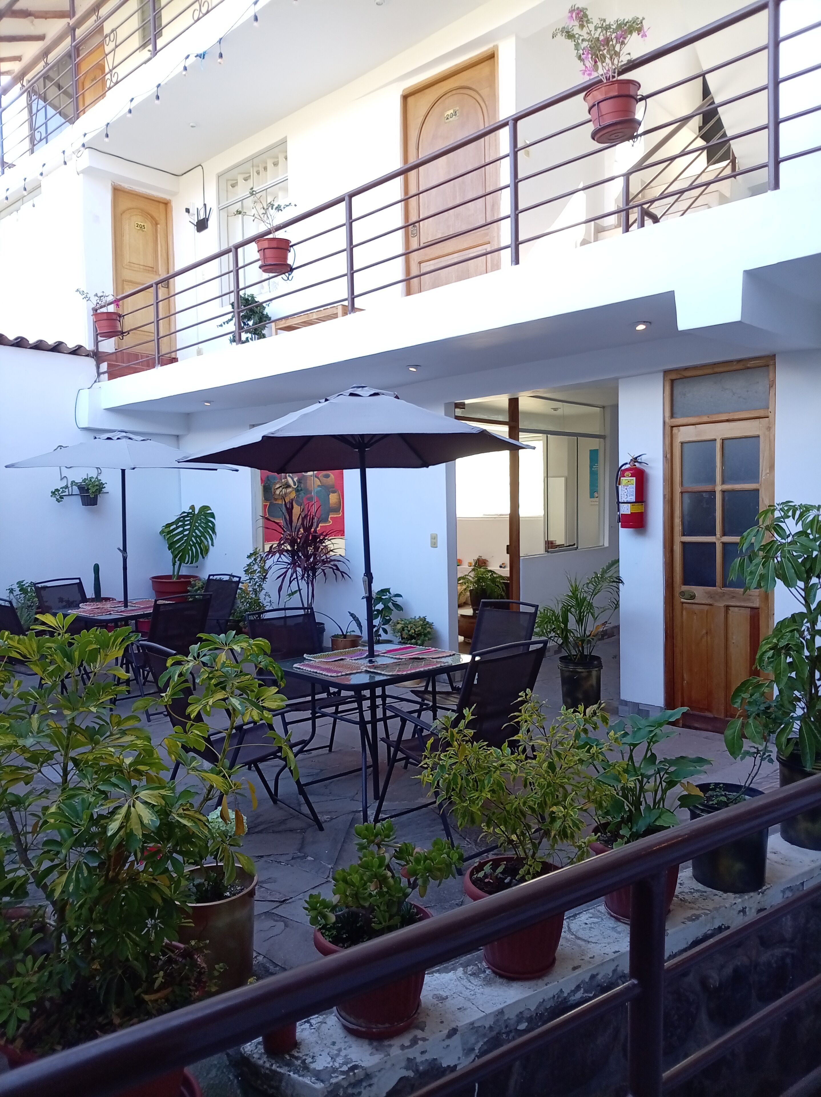 An outdoor seating area with tables and chairs, surrounded by potted plants.