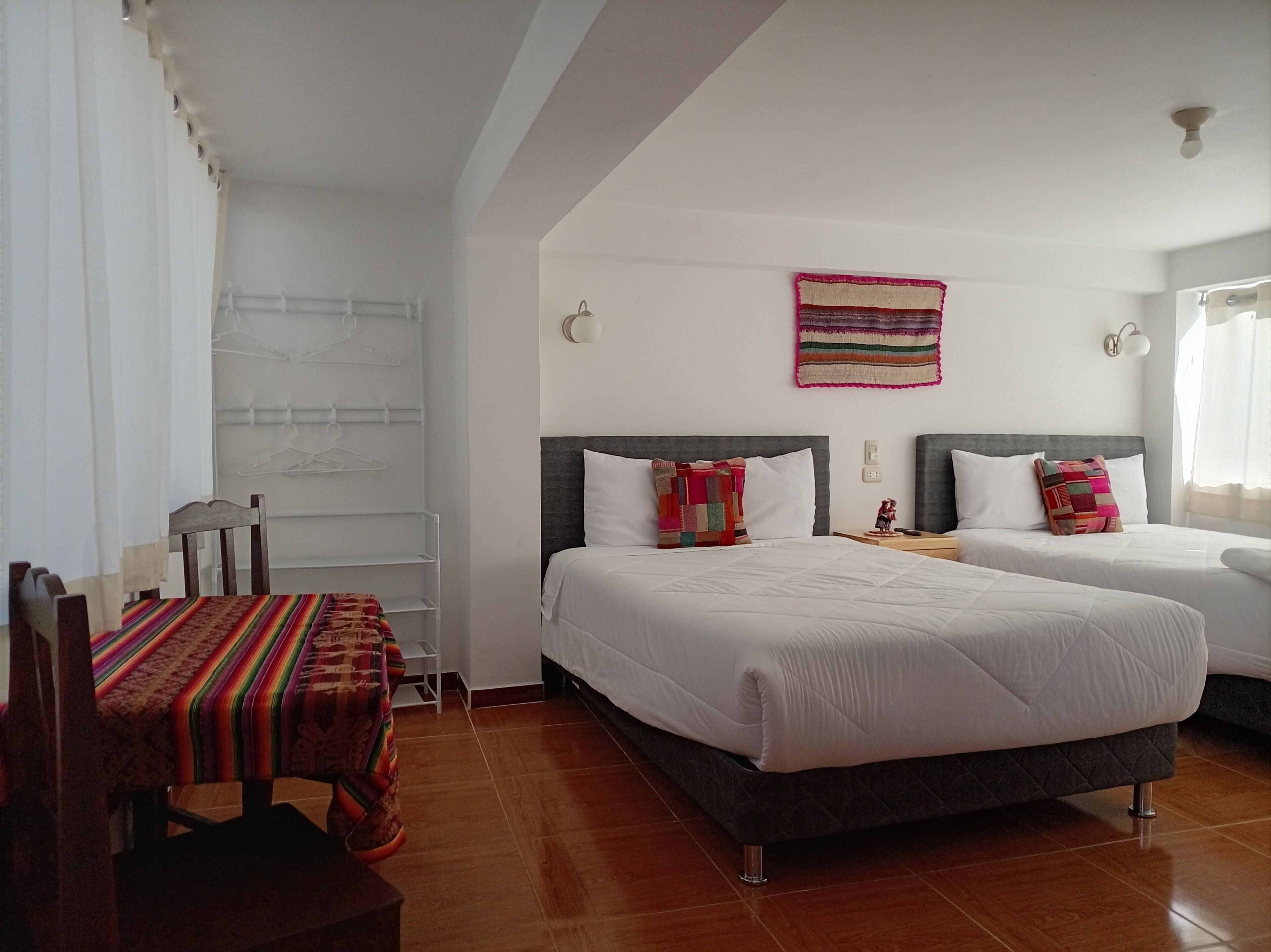 A hotel room with two beds, a chair, a table, and a wall-mounted rack.