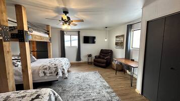 A room with bunk beds, a ceiling fan, a desk, a chair, and a television.