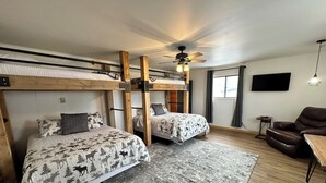 A room with two bunk beds, a ceiling fan, a TV, a brown leather chair, and a patterned rug. - Cozy 1-bedroom apartment unit C, sleeps 6  across from famous Cody Nite Rodeo! (Cody)