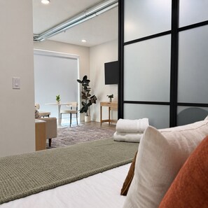 A modern hotel room with a bed, a desk, a chair, a television, and a large window.