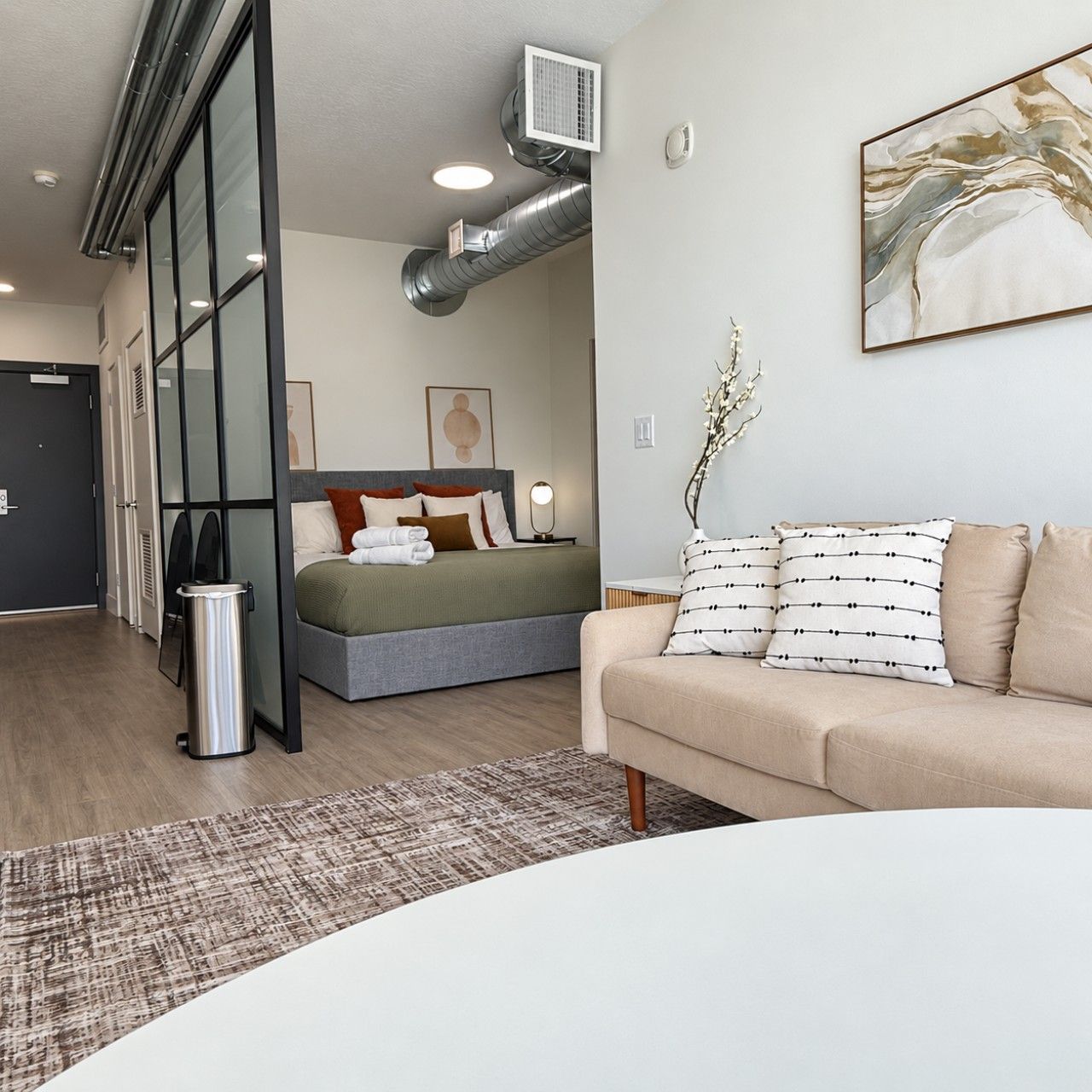 Ett modernt hotellrum med en säng, en soffa, en papperskorg och en tavla på väggen.