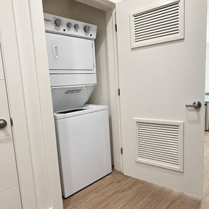 Une buanderie équipée d’un lave-linge et d’un sèche-linge superposés, d’une porte dotée d’une grille d’aération et d’un plancher en bois.