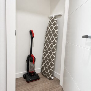 Une pièce contenant un aspirateur, une planche à repasser à motifs et une serviette blanche posée sur un étendoir.