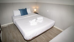 A neatly made bed with white linens and rolled towels, a blue pillow, and a bedside lamp on a wooden nightstand. - Apartment Duplo 08 (Madrid)