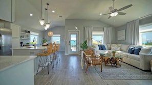 A modern kitchen with a dining area, a living room with a sofa and coffee table, and a ceiling fan. - Sleeps 24 2 Homes, Priv Pool, Swing Bar, Patio Lounge Near Nature Preserve (Port Aransas)