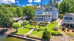 A multi-story house with a large front lawn, a dock, and a pond.
