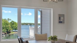 A dining area with a view of a lake, a white railing, and a potted plant.