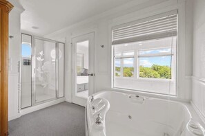A bathroom with a bathtub, a shower, and a window with blinds.