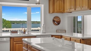 A kitchen with wooden cabinets, a large window with a view of a lake, and a sign that says 'Life is Beautiful.'