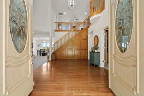 A spacious hallway with wooden flooring, a wooden staircase, and a view into a dining area.