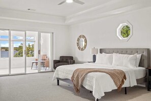 A bedroom with a large bed, a chair, a nightstand, and a view through a sliding glass door.