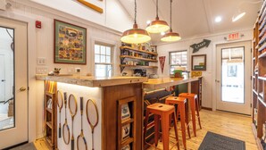 A cozy bar area with wooden bar counter, multiple tennis rackets displayed, and a sign indicating the exit. - Camp DeForest (Lincolnville)