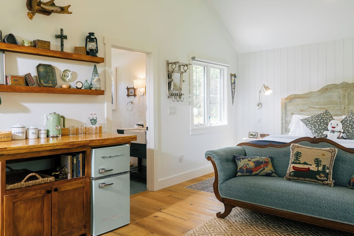 A cozy room with a wooden cabinet, a vintage-style sofa with patterned cushions, and a bed with a wooden headboard.