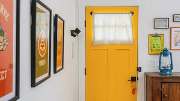 Una puerta amarilla con una cortina a rayas, carteles enmarcados en la pared, un mueble de madera con un farolillo y un llavero pequeño.