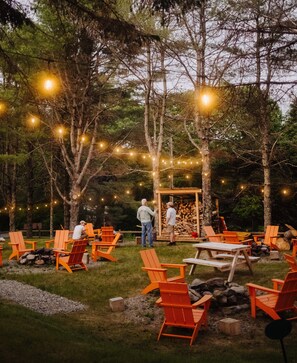 An outdoor seating area with orange chairs and tables, surrounded by trees and string lights. - Camp DeForest (Lincolnville)