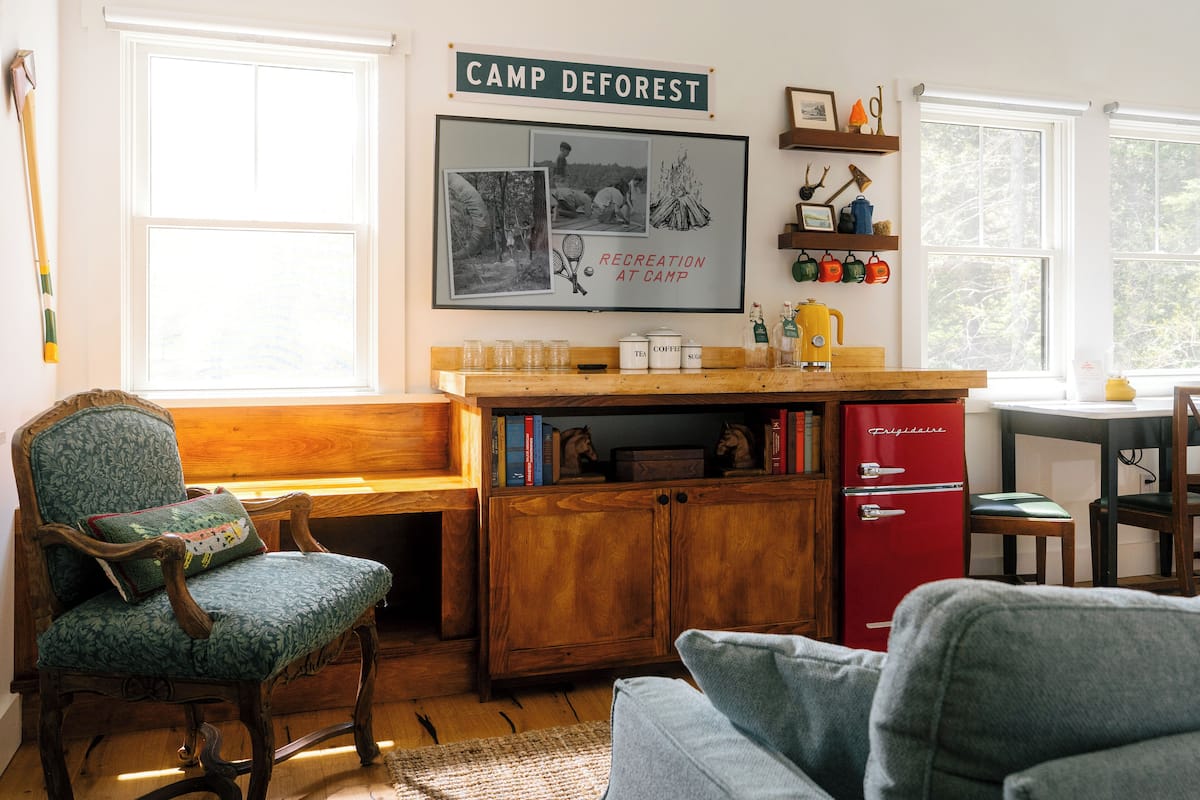 A cozy cabin interior with a wooden desk, a red refrigerator, and a large poster on the wall.