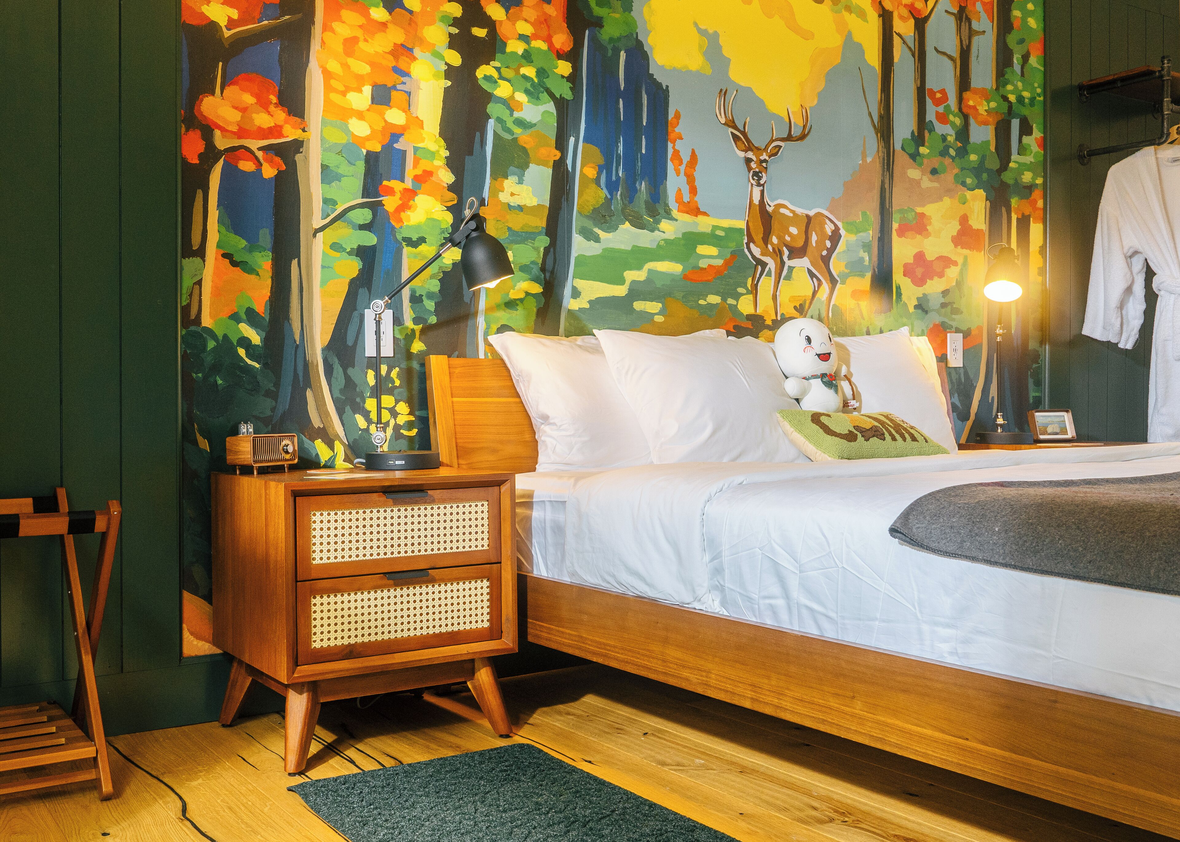 A bedroom with a bed, nightstand, lamp, and a wall mural.