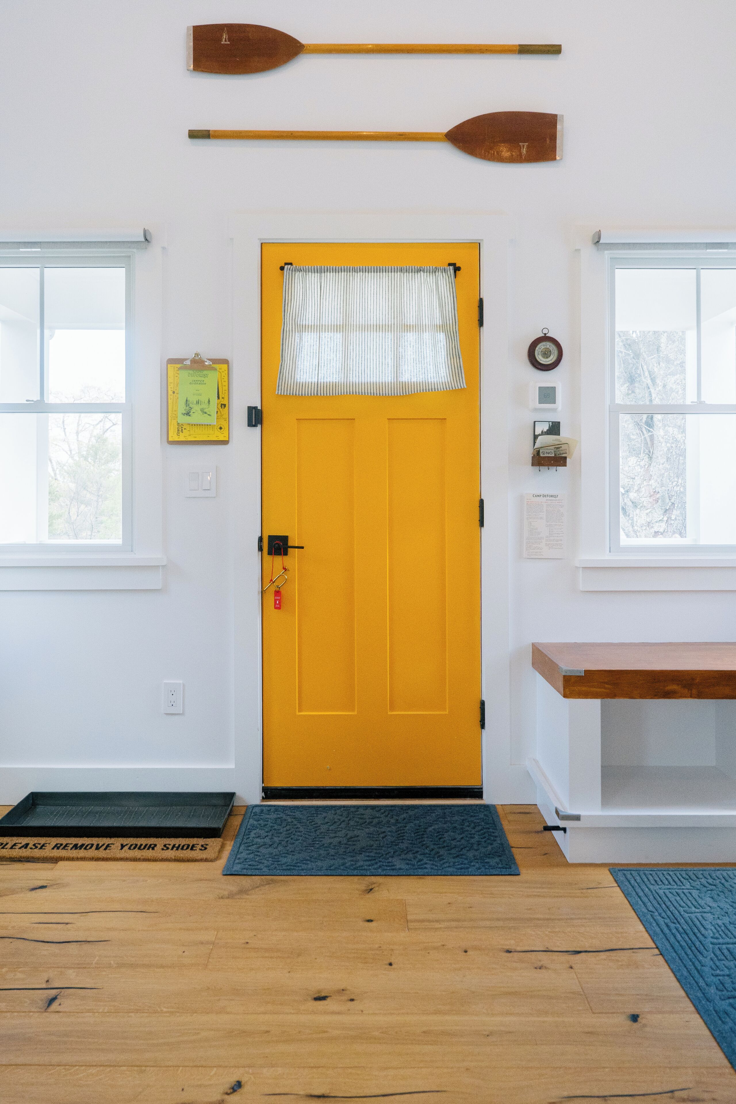 A bright yellow door with a window above it, a wooden paddle on the wall, and a small shelf with a clock.