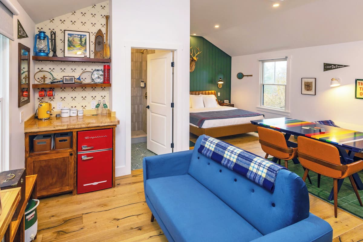 A cozy room with a blue sofa, a wooden dining table, and a bed with a green headboard.