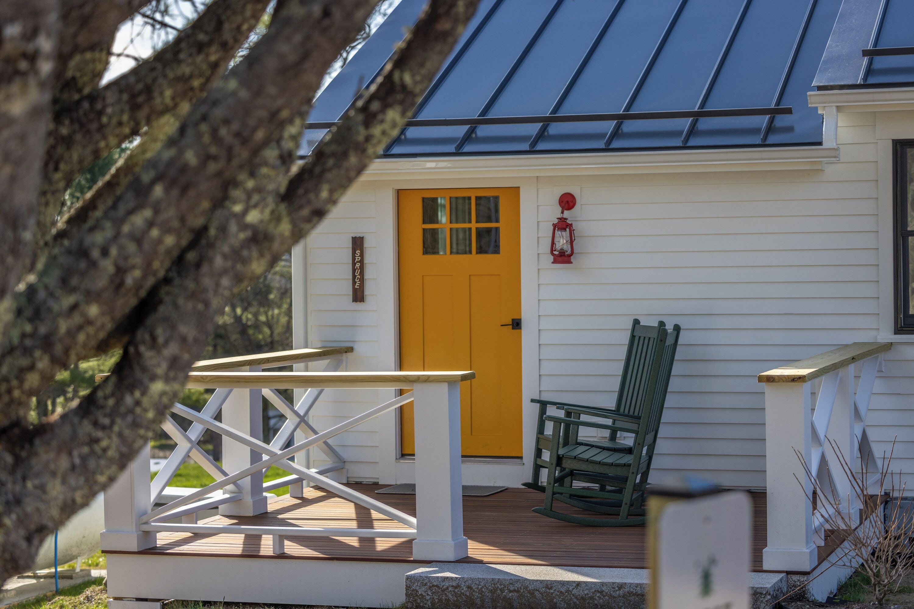 A wooden deck with a white railing, a yellow door, and a green rocking chair.