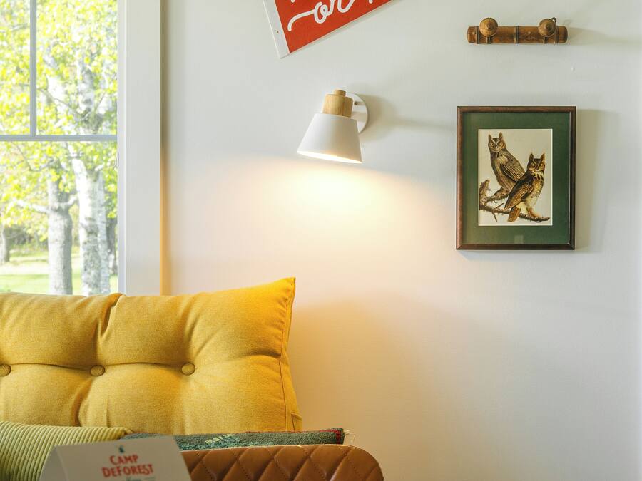 A room with a yellow pillow, a framed picture of owls, a 'Now or Never' sign, and a lamp.