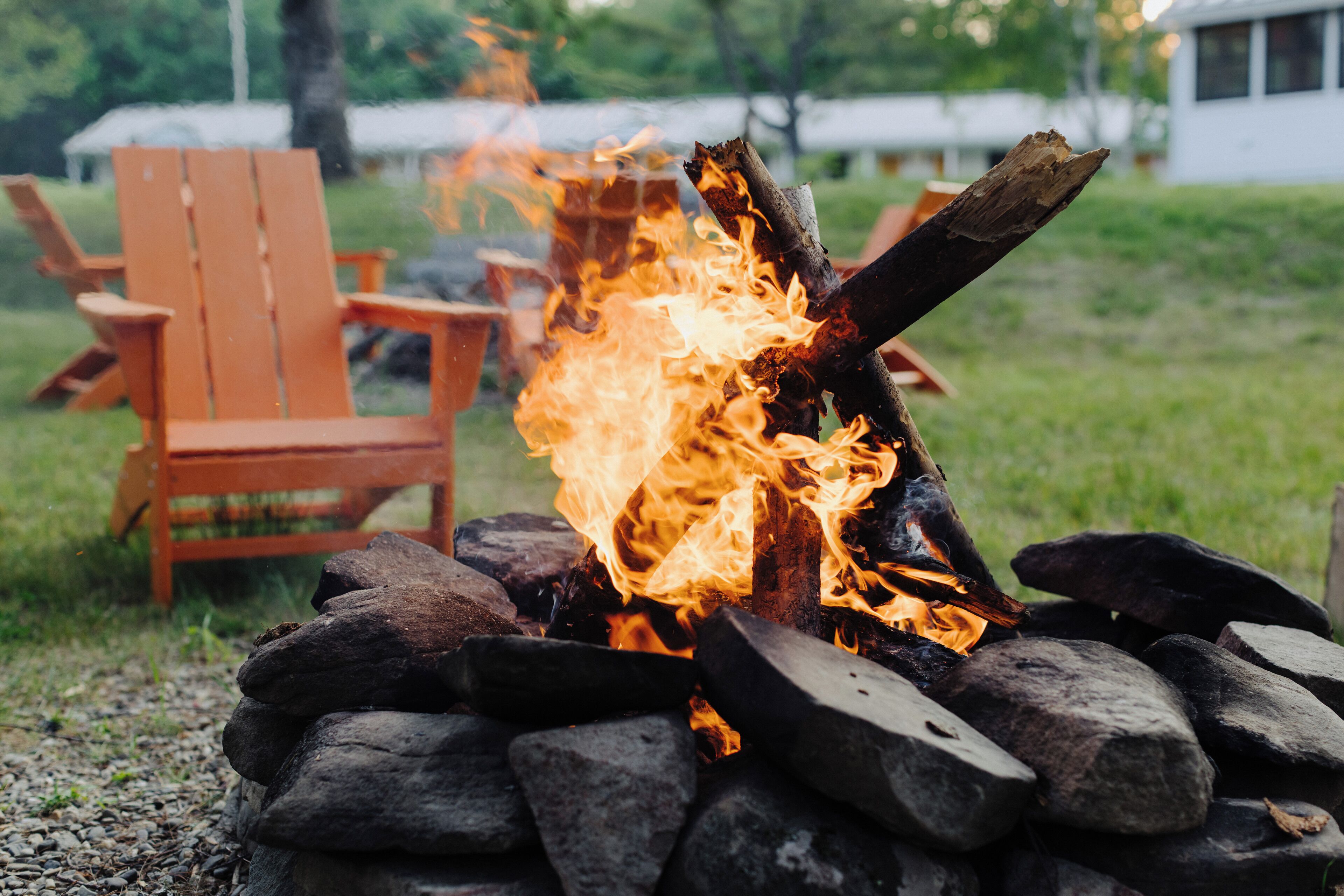Un feu de camp avec des bûches et des pierres, entouré de meubles d’extérieur.