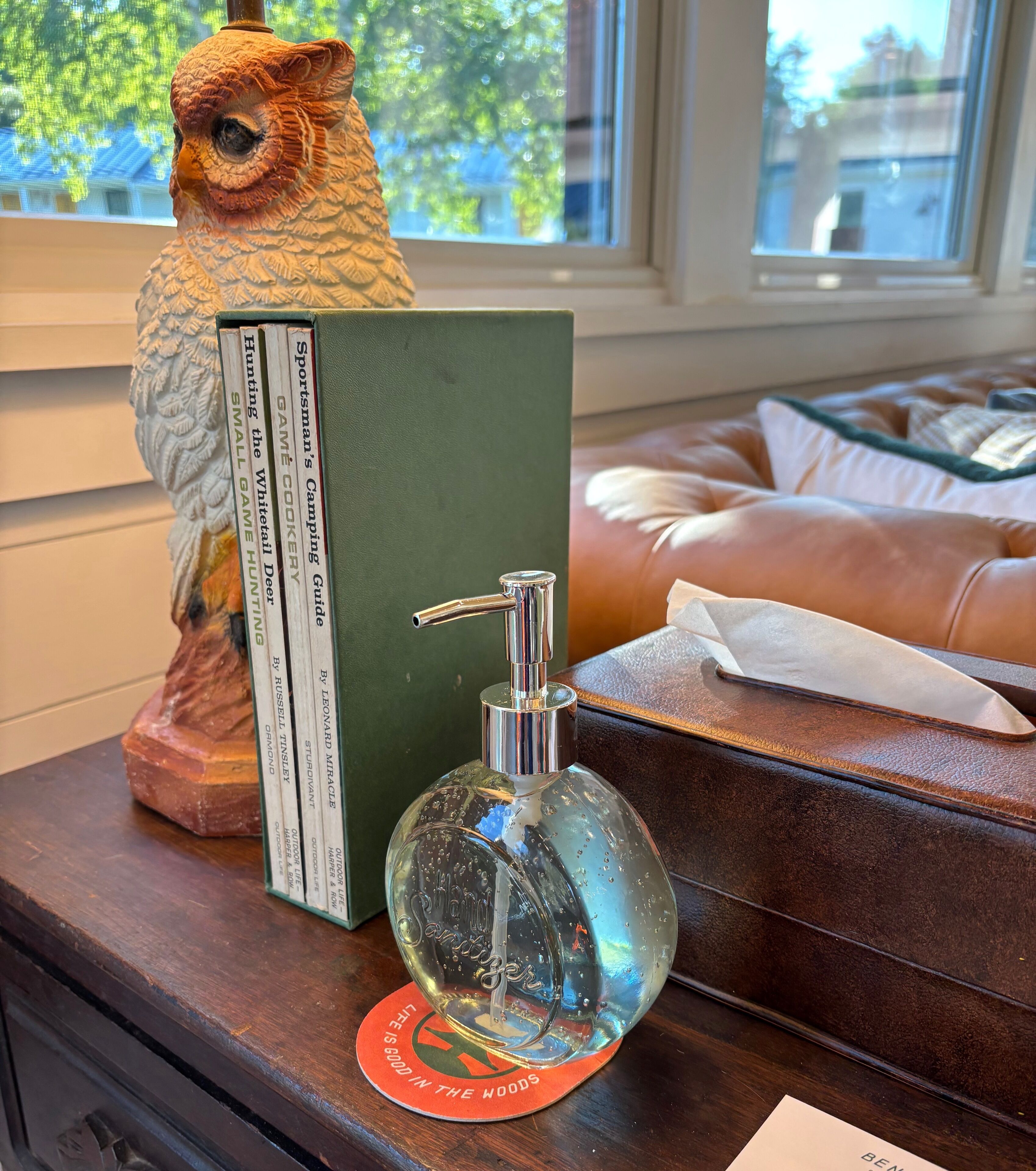Una mesa de madera con una botella de vidrio transparente, un libro verde y una figura decorativa de un búho.