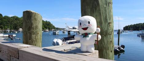 A wooden dock with a large white statue of a smiling bear holding a sign, surrounded by boats and a clear blue sky.