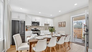 Une cuisine moderne avec des meubles blancs, des appareils en acier inoxydable et un coin repas comprenant une table en bois et des chaises blanches.