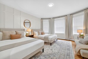 A modern bedroom with two beds, a large mirror, and a patterned rug.