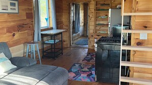 Un intérieur de chalet chaleureux avec un canapé, une table à manger, un coin cuisine et un escalier.